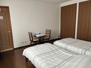 A hotel room with two beds, a small table with a chair, and a wardrobe. - MORE&MORE (Sakura)