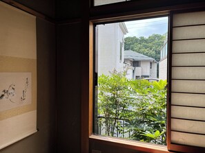 A room with a window overlooking a residential area, a wall with a framed artwork, and a door with a wooden frame. - MORE&MORE (Sakura)
