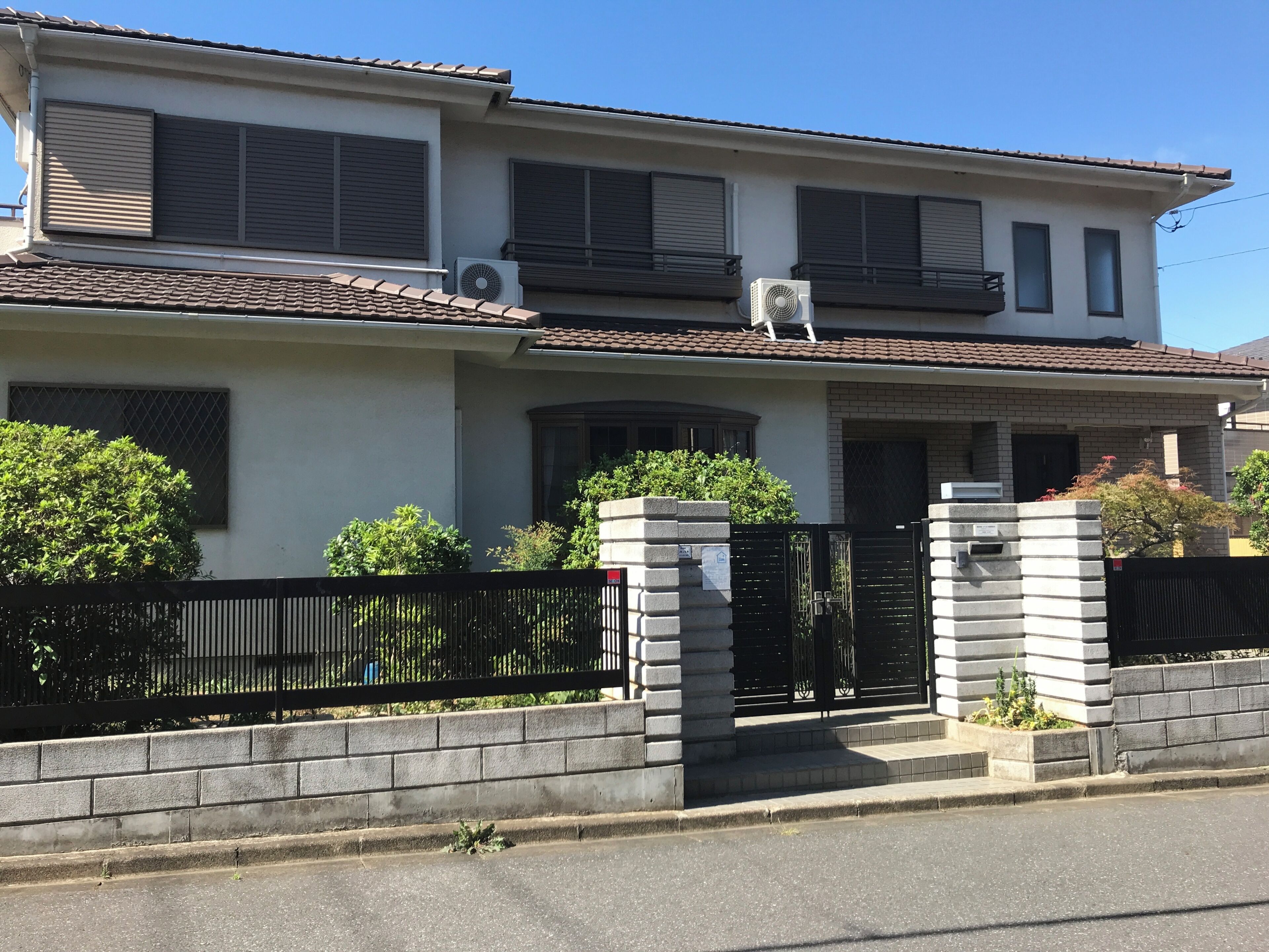 A two-story residential building with a tiled roof, a gated entrance, and a small balcony on the upper floor.