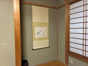 Une pièce dotée d’un sol recouvert de tatamis, d’un paravent en papier de riz (shoji) et d’un rouleau calligraphié suspendu au mur.