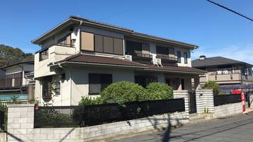 A two-story residential building with a flat roof, a balcony on the upper floor, and a gated entrance.