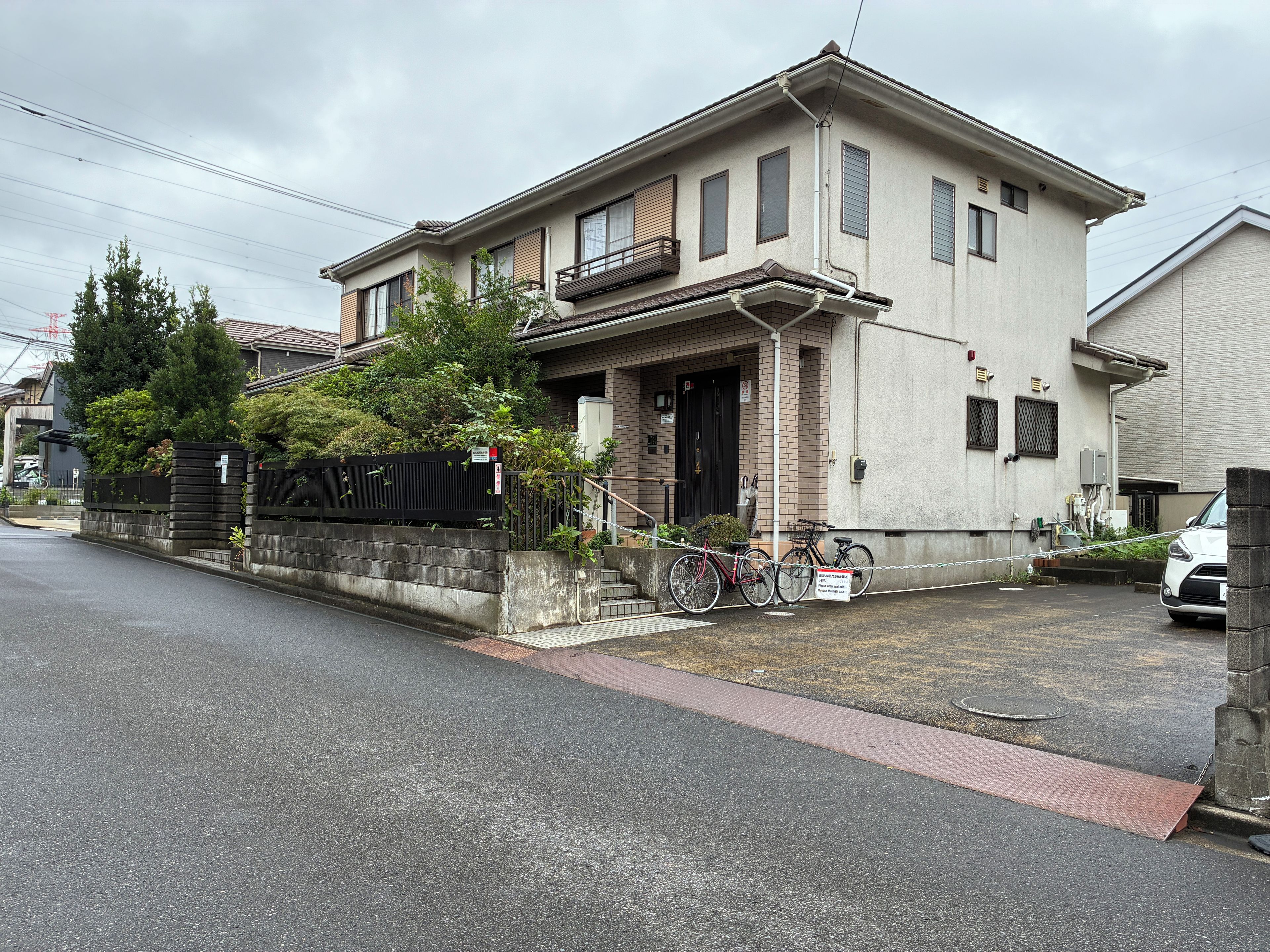 A residential building with a gated entrance, a bicycle parked outside, and a white car parked in the driveway.