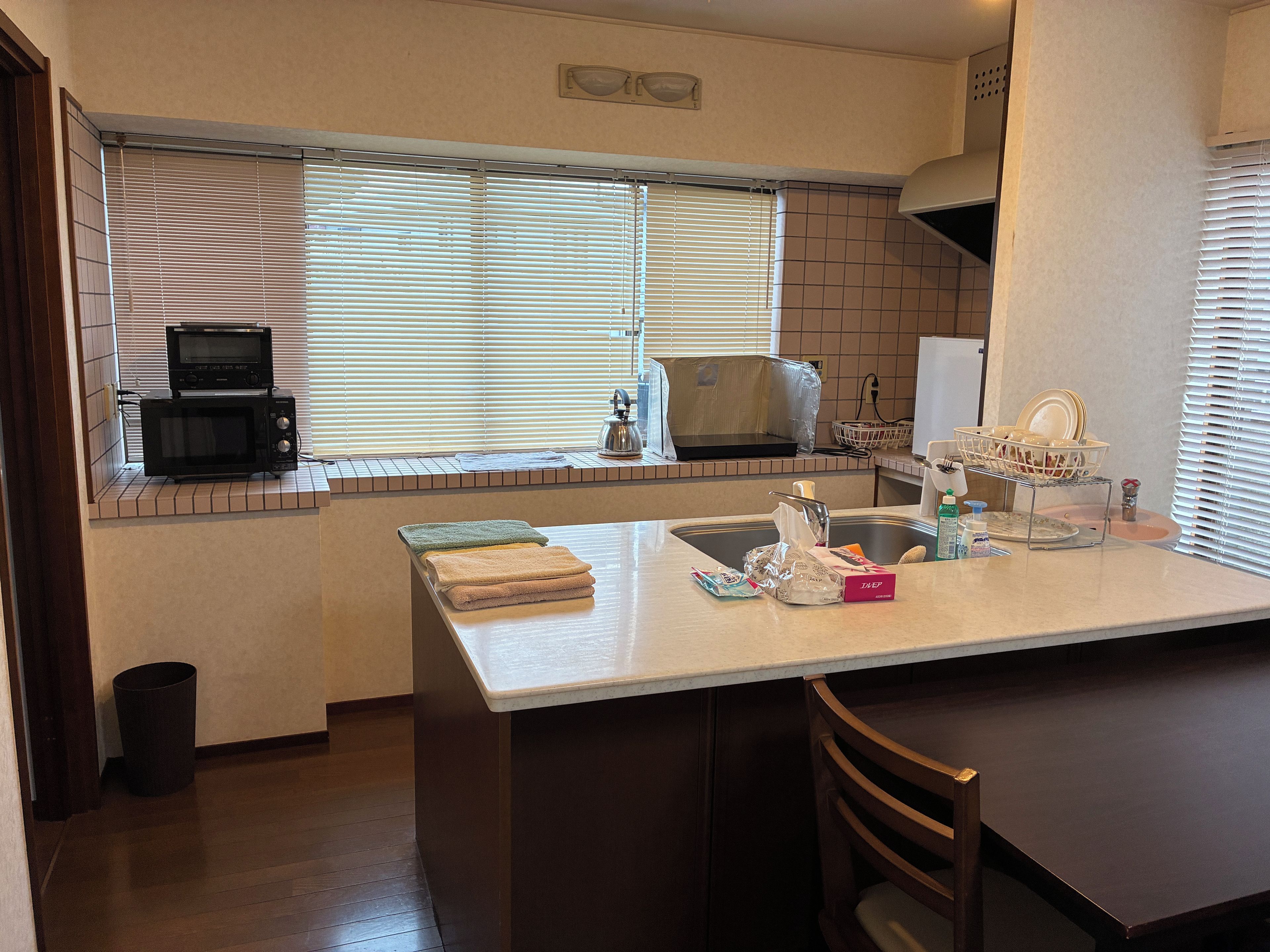 A kitchen with a microwave, a sink, and a window with blinds.