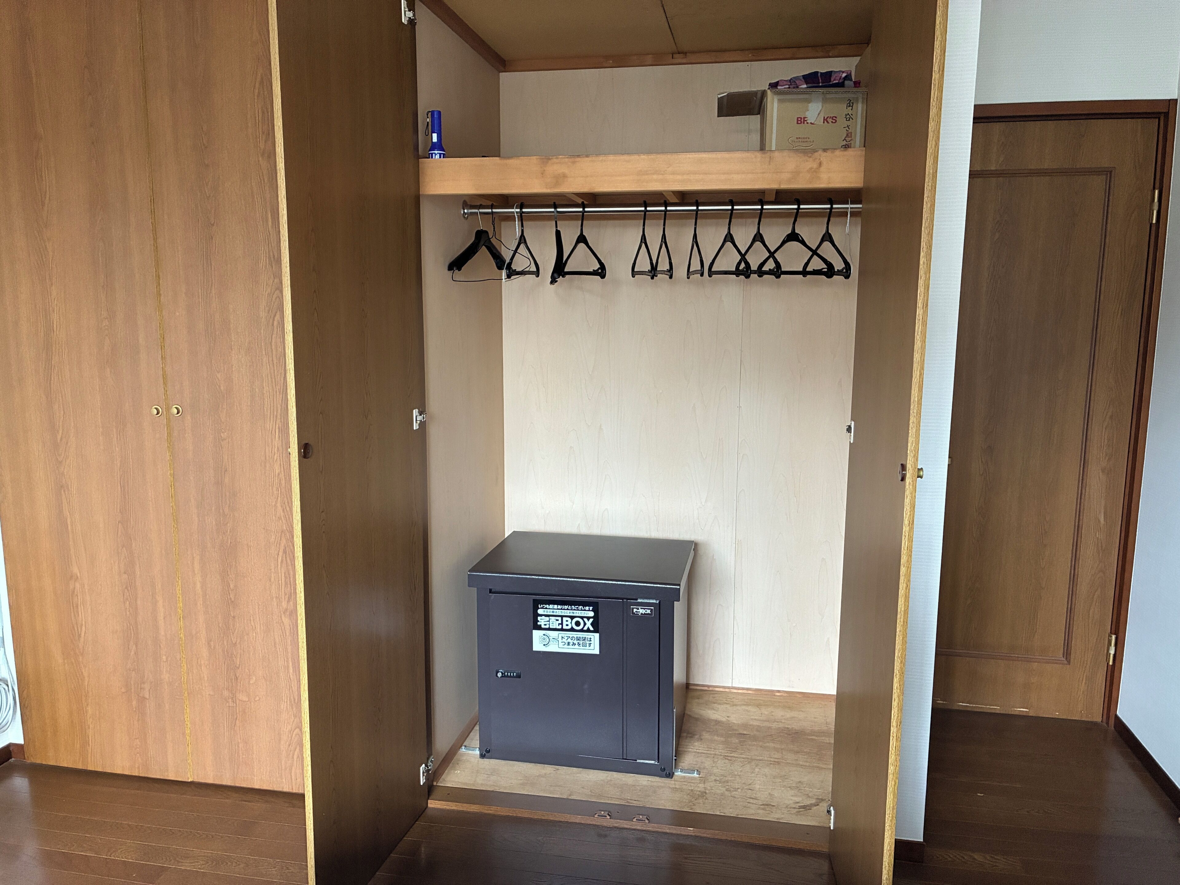 A walk-in closet with a wooden wardrobe, a metal storage box, and a clothing rack.