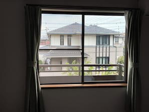 A window with a view of residential buildings, curtains, and a balcony. - MORE&MORE (Sakura)