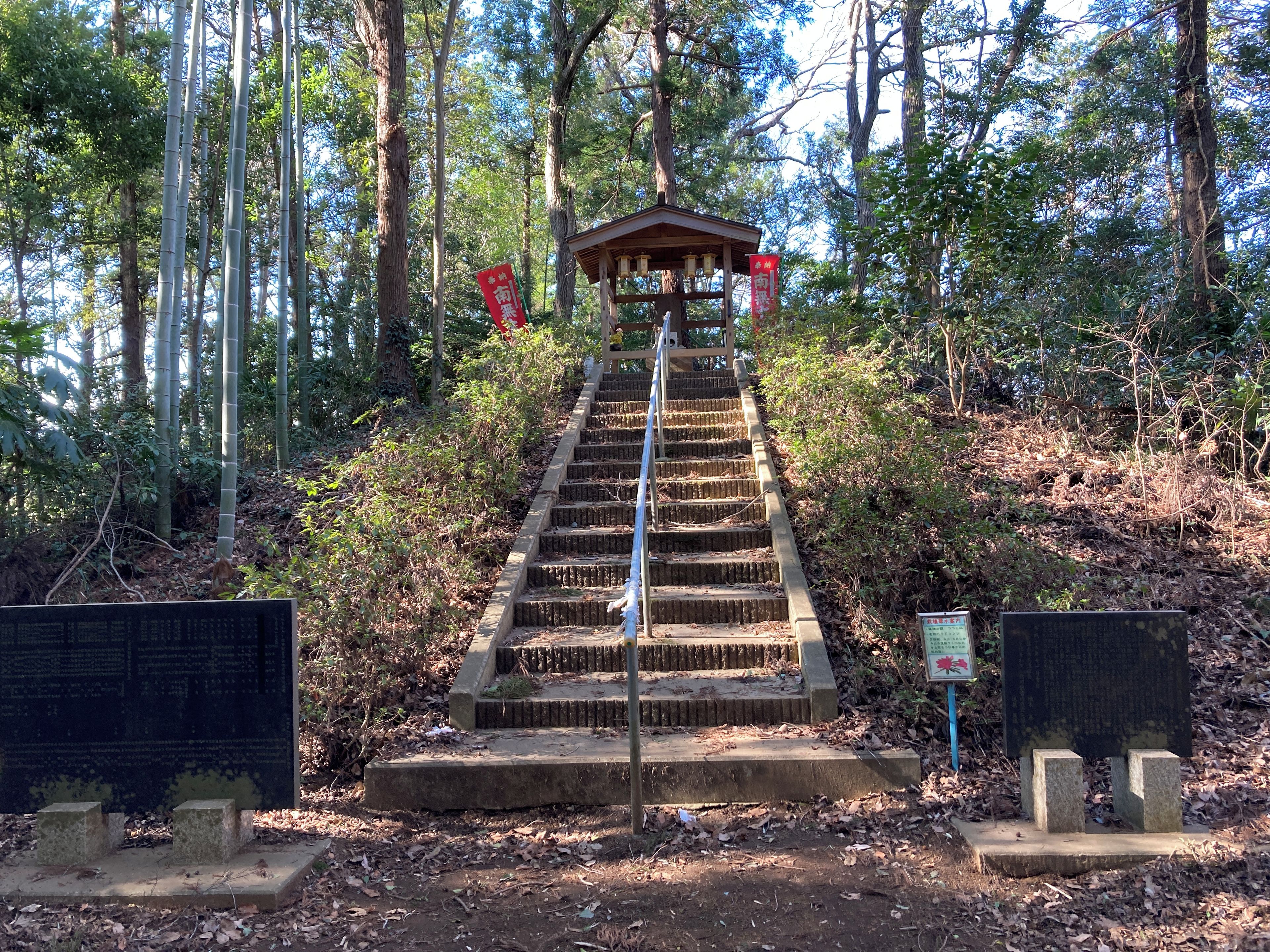 A stone staircase leading to a wooden structure in a forested area with red banners.