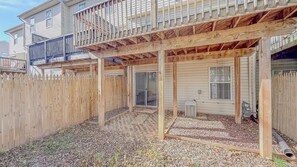 A covered outdoor area with a wooden deck, a fenced backyard, and a building with a garage.