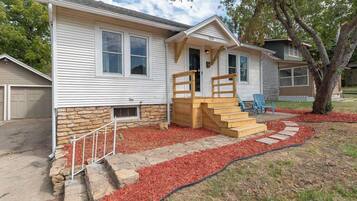 A single-story house with a stone foundation, a front porch with a wooden staircase, and a red mulch pathway leading to the entrance.