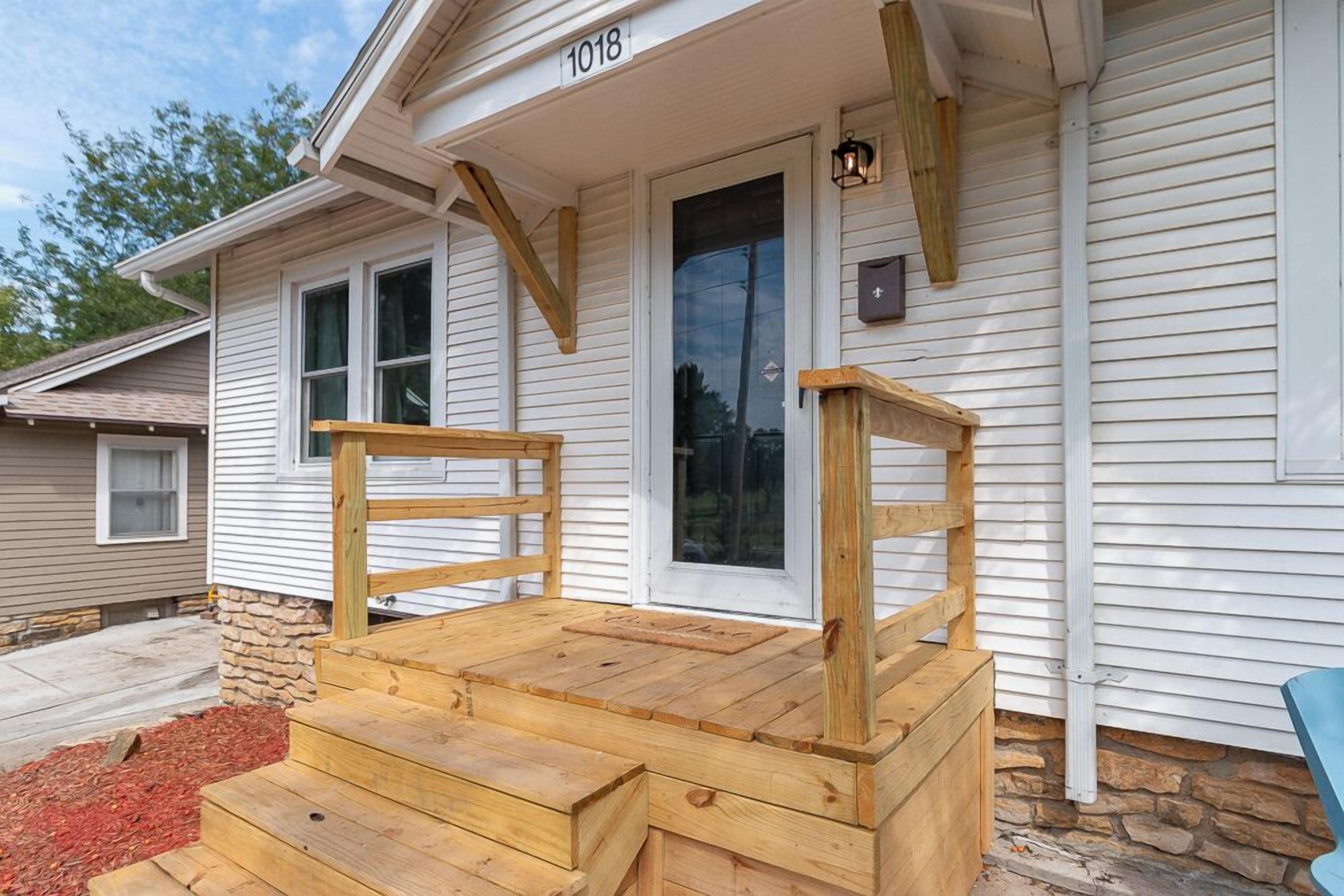 A wooden front porch with steps leading to a door, a mailbox, and a house number 1018.