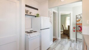 Cocina con electrodomésticos blancos, estufa y refrigerador. Hay un estante con objetos y un cartel en la pared.
