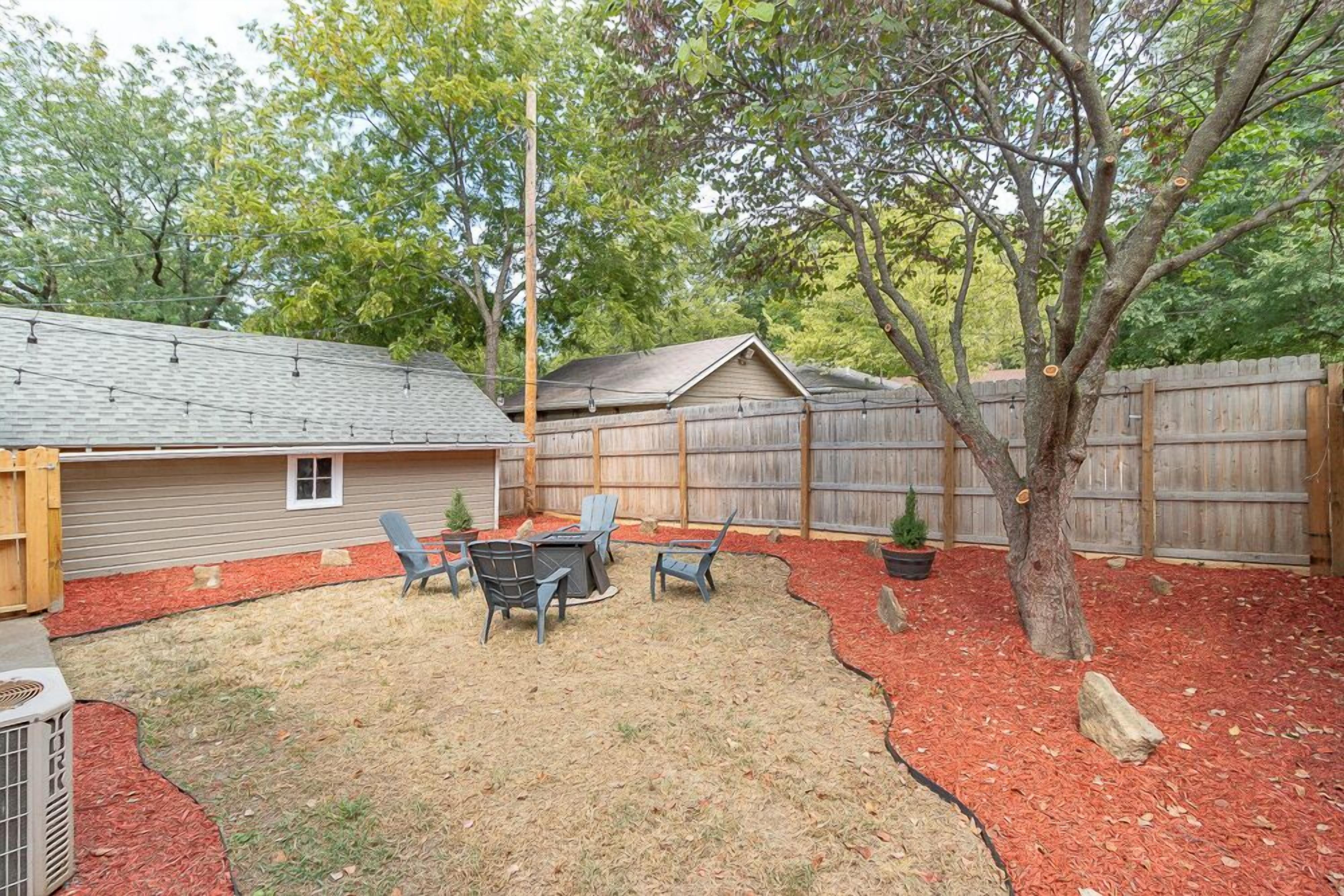 A backyard with a covered patio, outdoor seating, a tree, and a wooden fence.