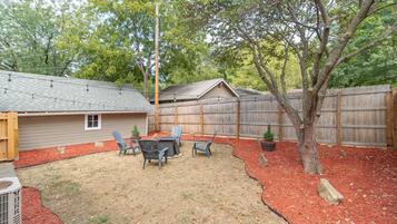 A backyard with a covered patio, outdoor seating, a tree, and a wooden fence.