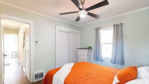 Un dormitorio con cama, ventilador de techo, ventana con cortinas, puerta y cómoda.