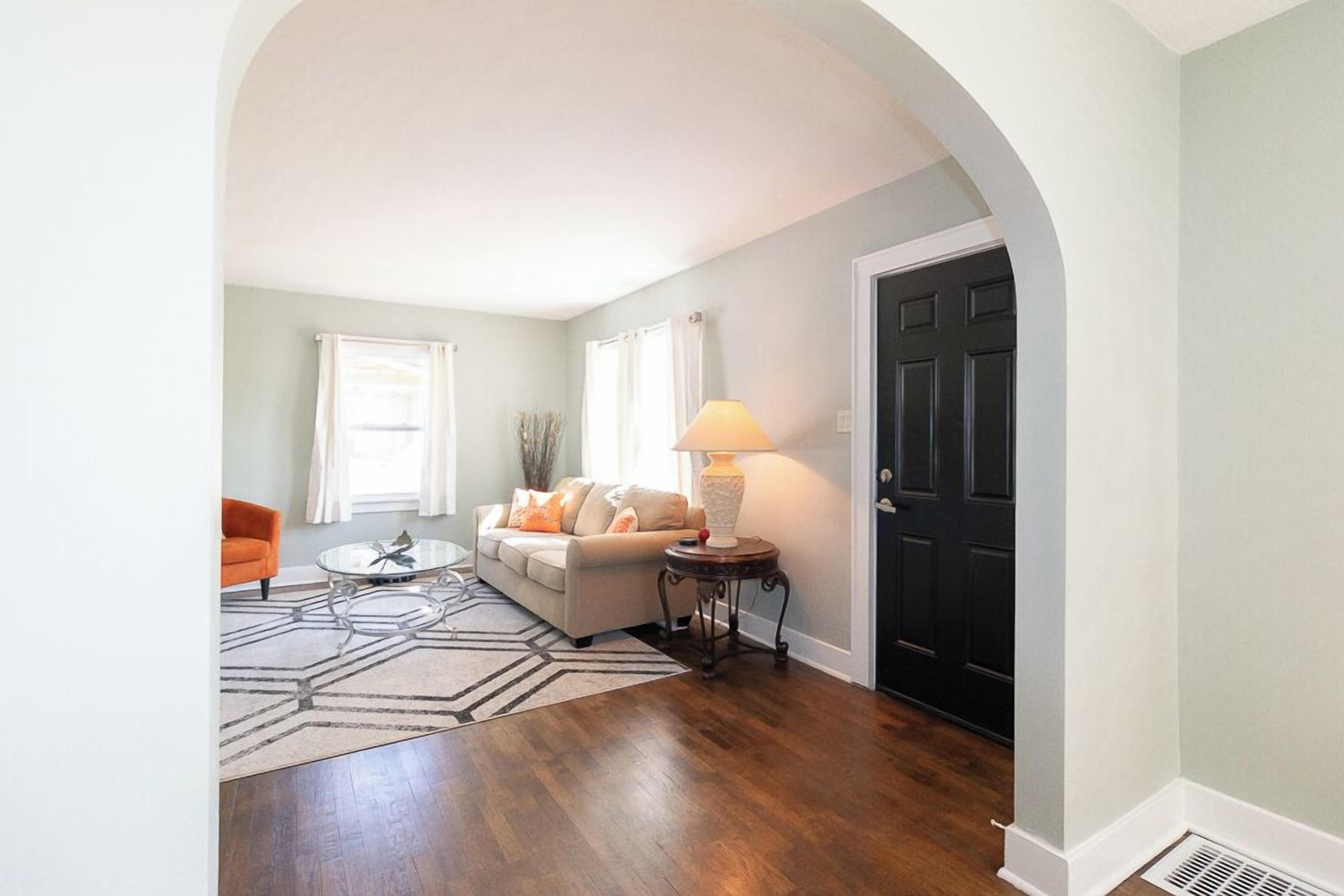 A living room with a sofa, coffee table, and lamp, a hallway with a door, and a patterned rug.