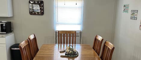 A dining room with a wooden table and chairs, a ceiling fan, a clock, and a window with blinds.