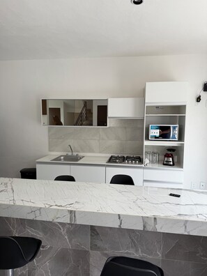 A modern kitchen with a marble countertop, white cabinetry, a built-in stove, and a microwave. - Private home with a pool, 5 minutes from Six Flags Oaxtepec (Jardines de Tlayacapan)
