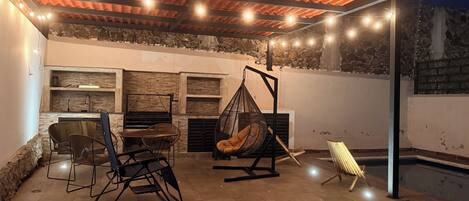 An outdoor patio with a stone wall, a hanging chair, and a table with chairs.