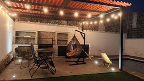 An outdoor patio with a stone wall, a hanging chair, and a table with chairs. - Private home with a pool, 5 minutes from Six Flags Oaxtepec (Jardines de Tlayacapan)