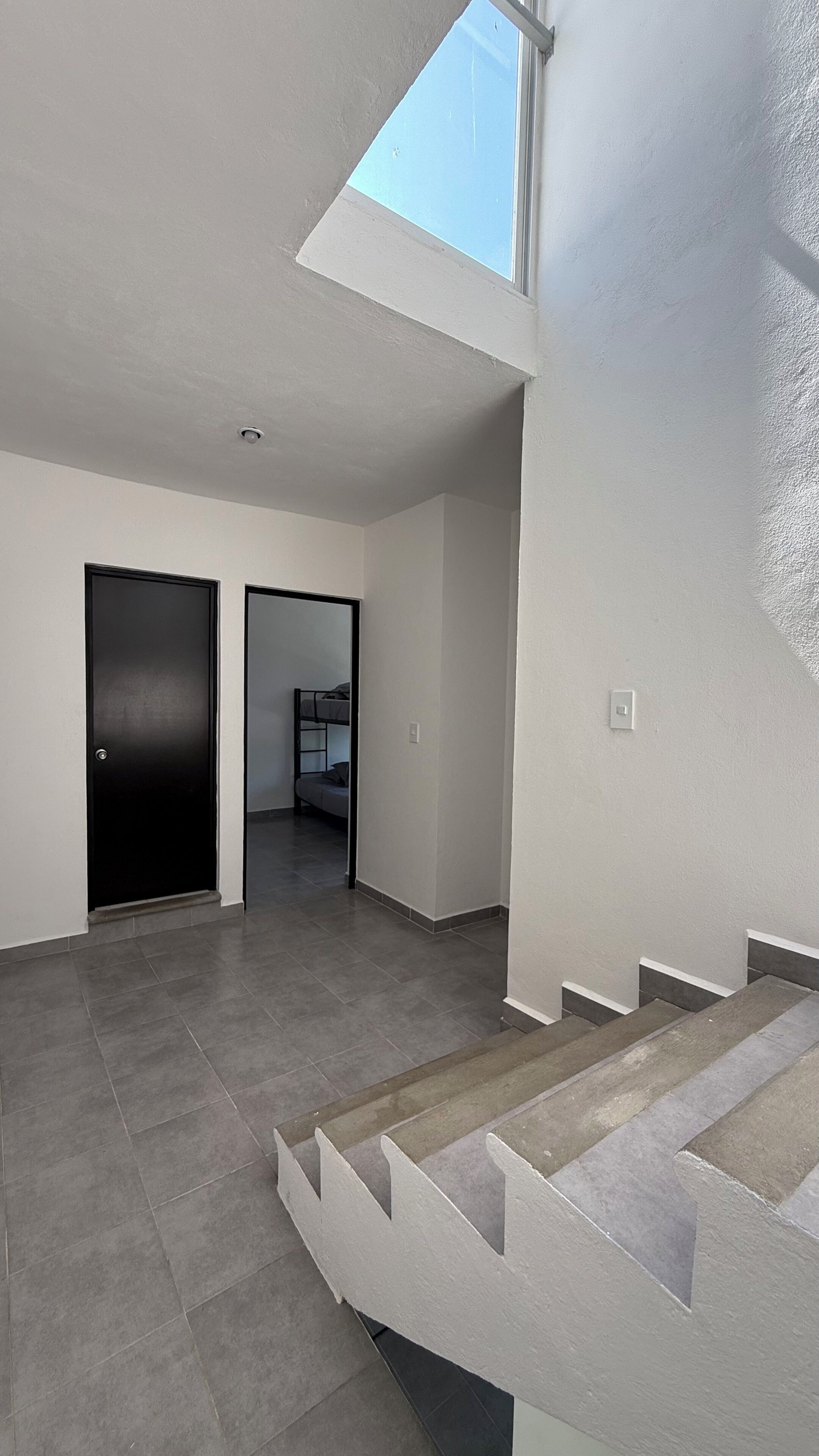 A modern interior with a staircase, a door, and a view of a room with a bunk bed.