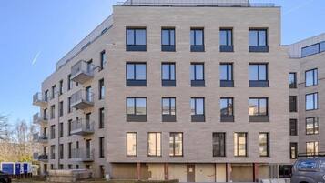Ein mehrgeschossiges Gebäude mit flacher Fassade, Balkonen und einem Parkplatz mit einem Fahrzeug.