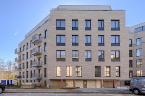 A multi-story building with a flat facade, balconies, and a parking area with a vehicle.