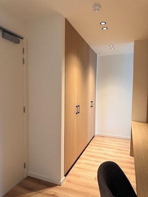 A hallway with a wooden wardrobe, a white door, and a desk with a chair. - Stay@brussels (Brussels)