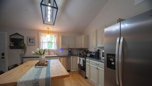 A modern kitchen with a central island, stainless steel appliances, and a window with curtains. - Charming outdoor getaway (Jay)