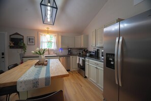 A modern kitchen with a central island, stainless steel appliances, and a window with curtains. - Charming outdoor getaway (Jay)