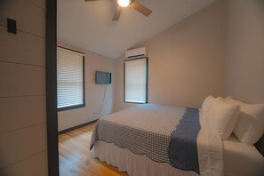 Una camera da letto con un letto, due finestre con persiane, un condizionatore d'aria e una ventola a soffitto.