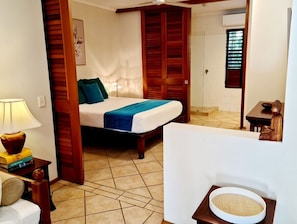 A bedroom with a bed, a bedside table with a lamp, a wooden door, and a small statue. - HIBISCUS DELIGHTS @ APARTMENT 19 - a lovely apartment in the heart of town. (Port Douglas)