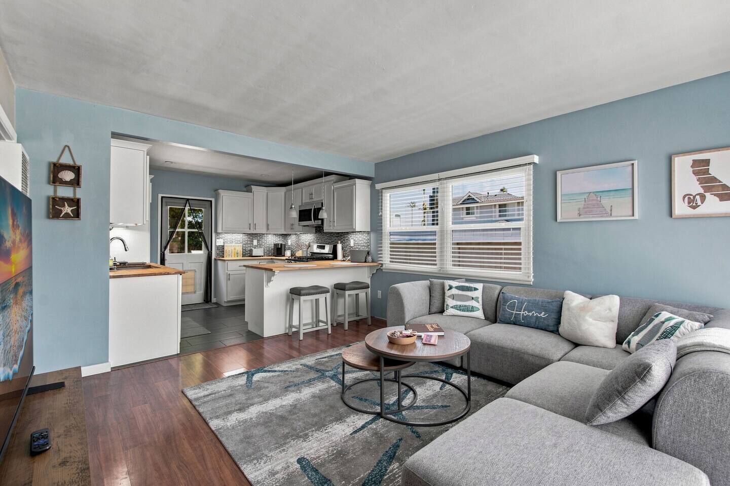 A modern kitchen with white cabinets, a central island, and a dining area with a gray sofa and a round coffee table.