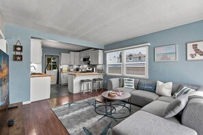 A modern kitchen with white cabinets, a central island, and a dining area with a gray sofa and a round coffee table.