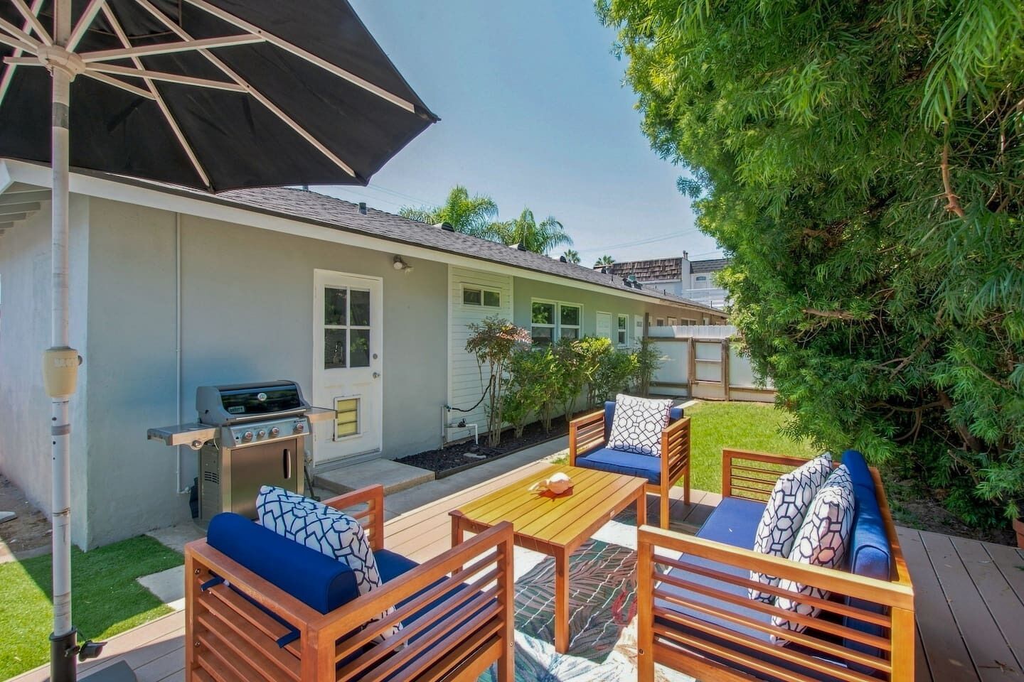 Une terrasse avec des meubles d’extérieur, un barbecue et un grand parasol.