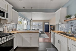 A modern kitchen with white cabinets, a wooden countertop, a built-in stove, and a large window.