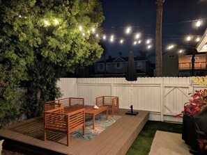 An outdoor deck with a wooden table and chairs, surrounded by a white fence and a tree.