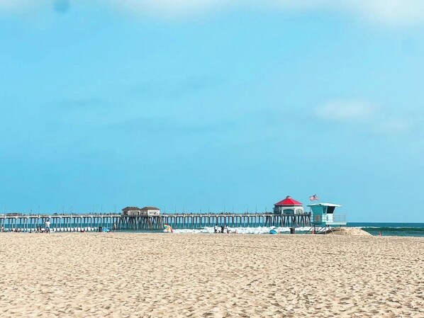A beach with a pier extending into the ocean, a lifeguard tower, and a clear sky.
