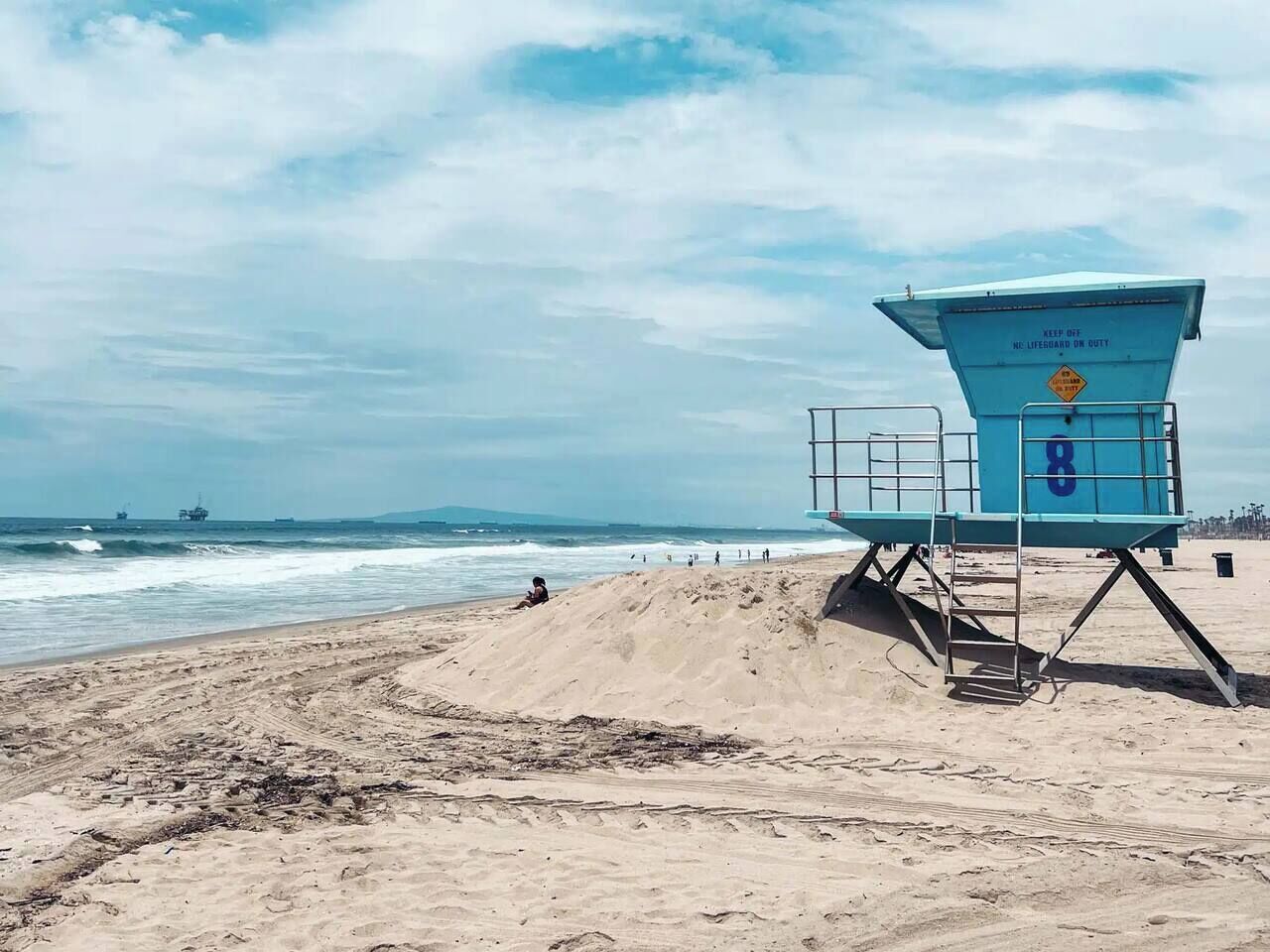 Une tour de surveillance avec le numéro 8, située sur une plage de sable, avec en arrière-plan l’océan et ses vagues.