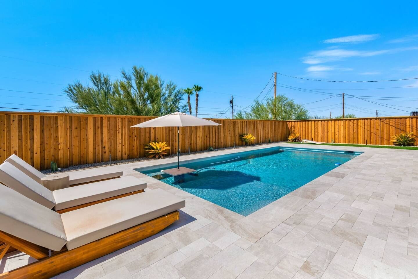 Ein rechteckiger Pool mit Holzzaun, Liegestühlen und einer gefliesten Poolterrasse.