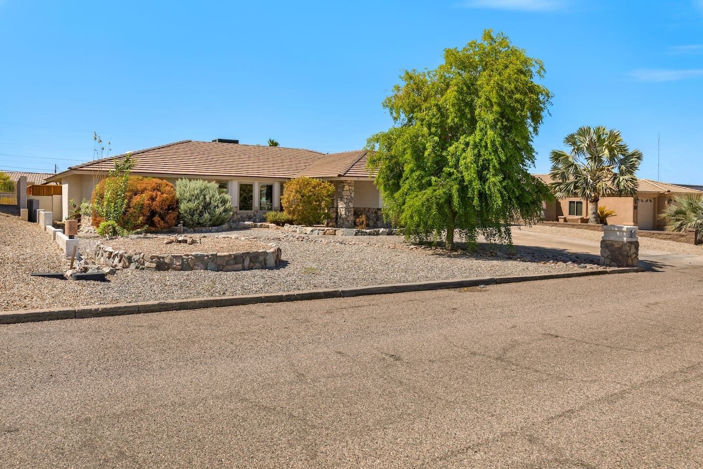 A residential property with a stone facade, a paved driveway, and a landscaped front yard with a tree and shrubs.