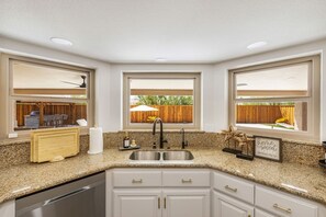 A kitchen with a granite countertop, a stainless steel sink, and white cabinetry. - Havasu Caravelle - Pool Table, BBQ, Bar, Ping Pong (Lake Havasu City)