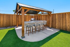 An outdoor barbecue area with a wooden pergola, a grill, and a bar stool seating arrangement. - Havasu Caravelle - Pool Table, BBQ, Bar, Ping Pong (Lake Havasu City)