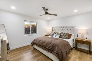 A bedroom with a tufted headboard, a large window, a ceiling fan, and a bedside table with a lamp. - Havasu Caravelle - Pool Table, BBQ, Bar, Ping Pong (Lake Havasu City)