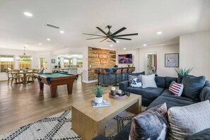 A spacious living room with a pool table, a dark-colored sofa, and a coffee table. - Havasu Caravelle - Pool Table, BBQ, Bar, Ping Pong (Lake Havasu City)
