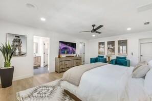 Ein modernes Schlafzimmer mit einem Bett, einem Deckenventilator, einem Fernseher und Kunstwerken an den Wänden.
