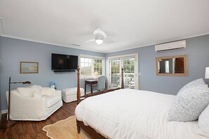Ein Schlafzimmer mit einem großen Bett, einem Schreibtisch, einem Stuhl, einem Fernseher und einem Balkon.