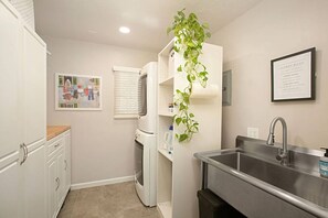 A compact kitchen with white cabinetry, a stainless steel sink, and a wall-mounted plant.