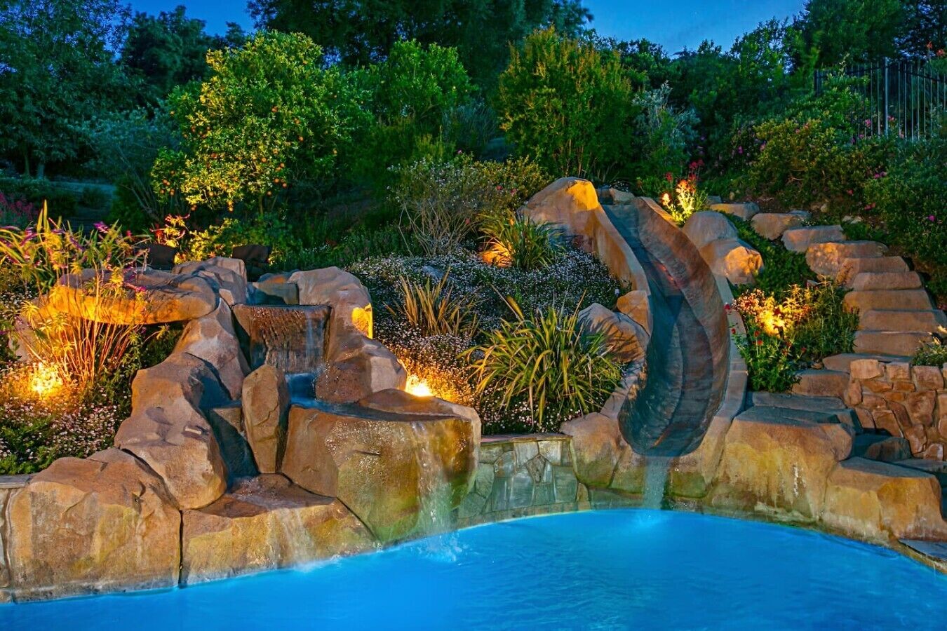 A swimming pool with a waterfall feature surrounded by rocks and plants.