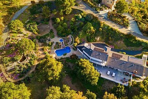 An aerial view of a property with a swimming pool, landscaped gardens, and a building with solar panels.