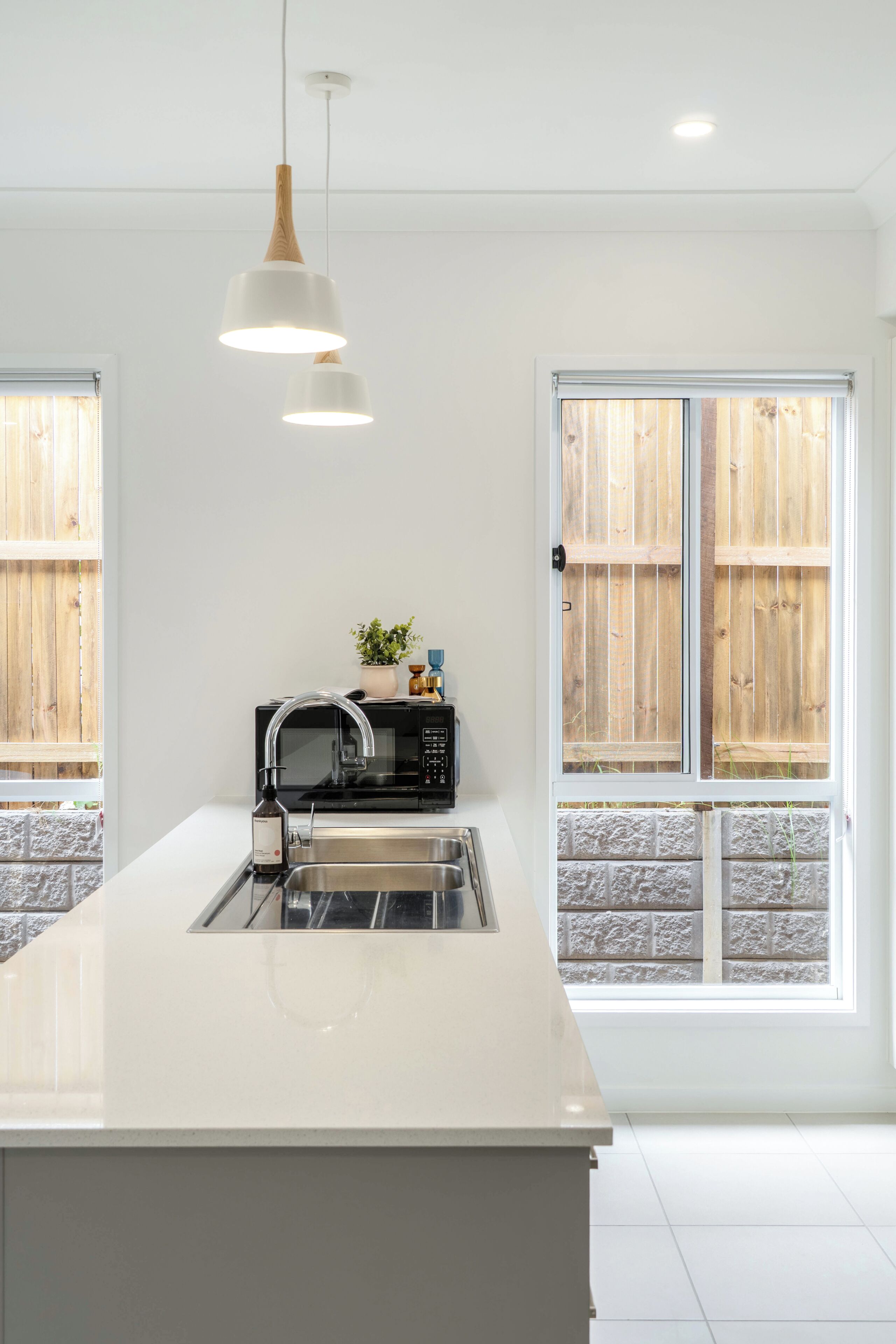 A modern kitchen with a central island, stainless steel appliances, and a view of a wooden fence through large windows.