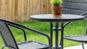 Une terrasse avec une table ronde et deux chaises, un pot de fleurs et une clôture en bois.